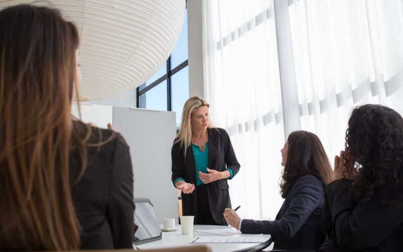 A business team in a modern office engaged in a presentation led by a woman, fostering teamwork and collaboration.