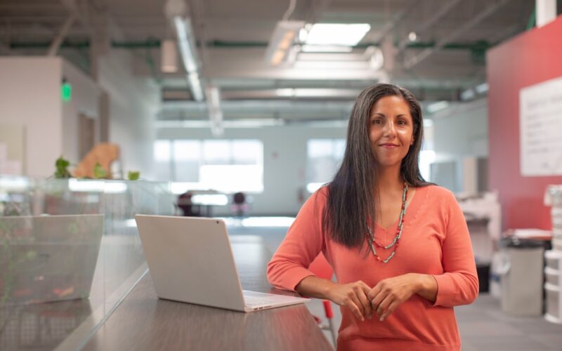 woman in orange long sleeve shirt sitting beside table with macbook pro